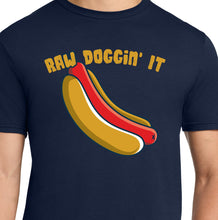 Load image into Gallery viewer, A man wearing a navy blue t-shirt with a graphic of a raw hot dog and the text 'RAW DOCCIN' IT' in a hot dog printed shirt, against a plain white background.